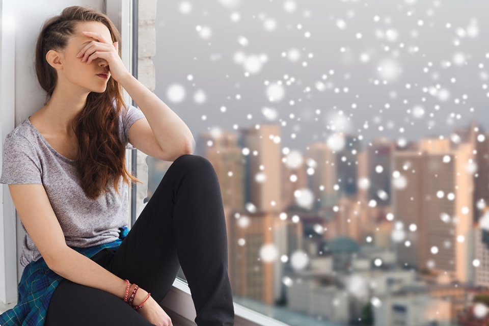 Woman sitting near window with grey snowy weather outside